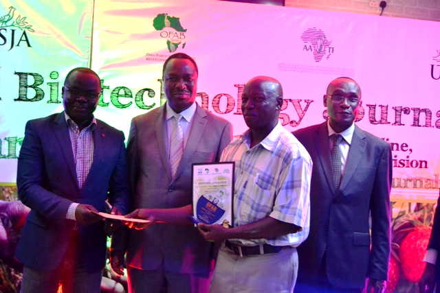 Lutaaya in chaquered shirt, receiving the a cash award from OFAB Africa Coordinator Mr. Daniel Otunge. S&T Minister Dr. Elioda Tumwesigye (2nd left) and UNCST Exec. Secretary Dr. Peter Ndemere witnessed the occasion 