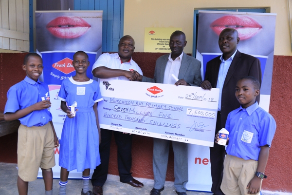 Vincent Omoth, Marketing Manager Fresh Dairy (L) hands over a dummy cheque worth 7.5Million UGX to Demayi Francis Parents' Representative at Murchison Bay Primary School
