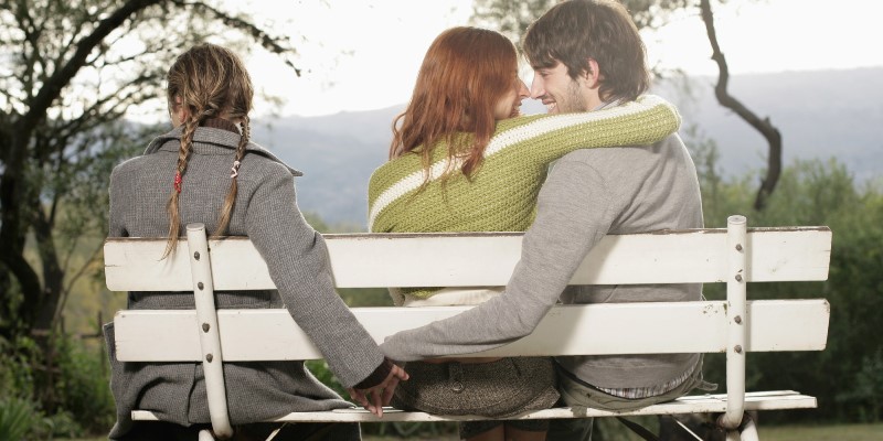 Couple embracing on bench, while man holds other woman’s hand