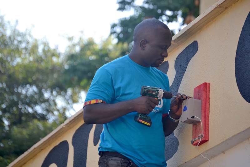 Joel-Ssematimba-AirQo-Embedded-Systems-Engineer-installing-an-AirQo-Air-Quality-Monitor-at-Jinja-City-Hall