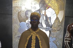 Master Ntakky stands proudly before his striking American Dream art piece, a fusion of bold colour and layered symbolism.